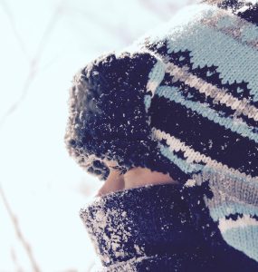 close up of child wearing scarf and tuque staring through fence in winter