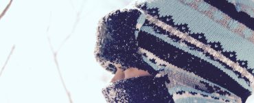 close up of child wearing scarf and tuque staring through fence in winter