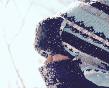 close up of child wearing scarf and tuque staring through fence in winter