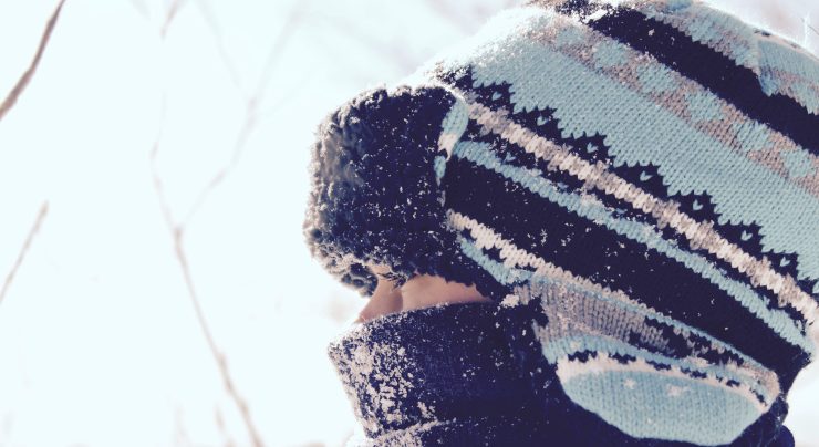 close up of child wearing scarf and tuque staring through fence in winter