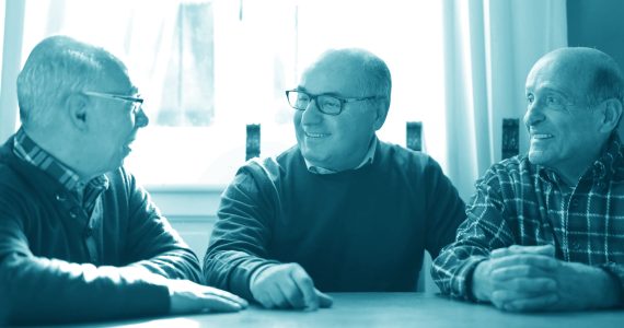 three older men sitting at a table, smiling