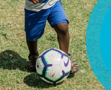 small child kicking soccer ball on grass